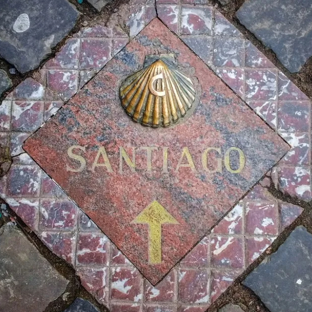 Santiago waymarker with a brass scallop shell and yellow arrow set into stone paving
