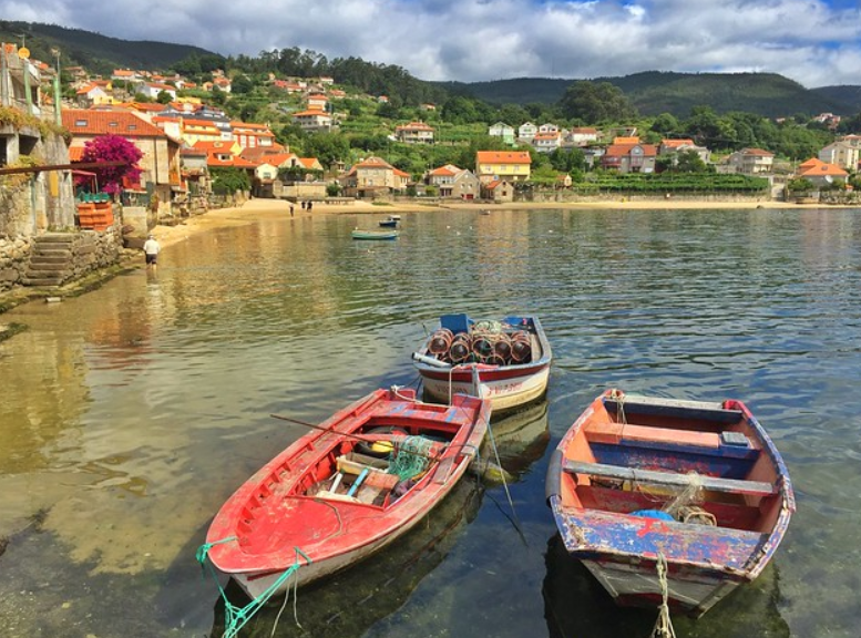 Colourful fishing boats in calm coastal waters beside a village of stone houses and red-tiled roofs